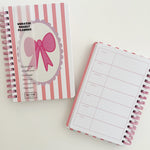 Two spiral-bound planners with pink and white design on a light background
